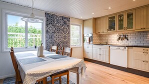 A modern kitchen with white cabinets, a wooden dining table, and a view of greenery outside. - 2 bedroom awesome home in Brastad (Brastad)