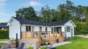 A white building with a dark roof, wooden deck, and outdoor seating area with chairs and tables. - 2 bedroom awesome home in Brastad (Brastad)