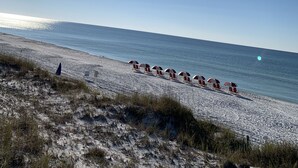 A beach with rows of red and white beach umbrellas and chairs, a clear sky, and the sun shining. - 5min Walk to Beach, Free Golf Cart, Pool, Luxe Townhome (Miramar Beach)