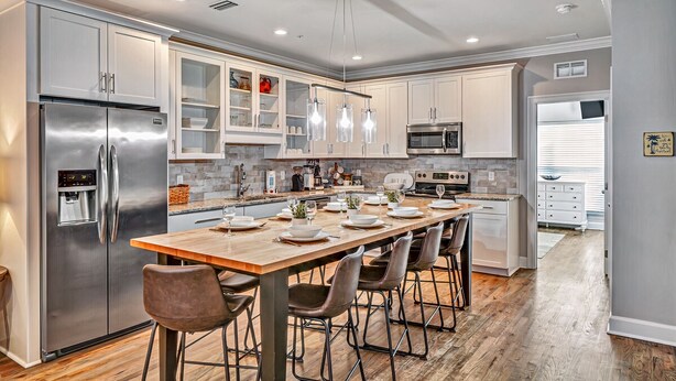 A modern kitchen with stainless steel appliances, a wooden dining table, and a large island with bar stools. - 5min Walk to Beach, Free Golf Cart, Pool, Luxe Townhome (Miramar Beach)