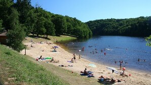 A beach with people swimming and sunbathing, surrounded by trees.