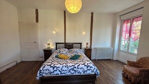 A bedroom with a large bed, wooden floor, two bedside tables with lamps, a radiator, and a window with curtains.