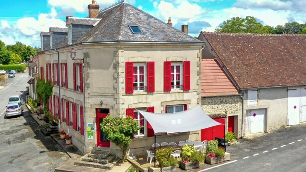 A two-story building with red shutters, a sloped roof, and a small balcony.