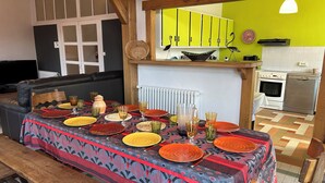A dining area with a table set for six, a sofa, a kitchen in the background, and a bright green wall.