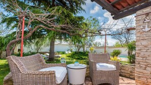 Un espace patio aménagé avec des meubles en osier et une petite table, entouré de verdure et bordé d’un mur en pierre.