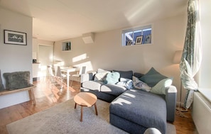 Ein modernes Wohnzimmer mit einem grauen Sofa, einem kleinen Holztisch und einem Essbereich im Hintergrund.