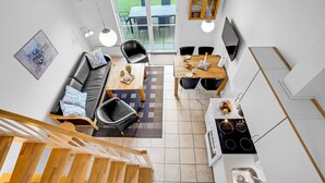 Eine moderne Küche mit Einbauherd, eine Essecke mit Tisch und Stühlen, ein Sofa mit Kissen und eine Treppe, die zu einer oberen Etage führt.