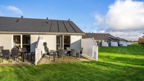 Ein Wohngebäude mit Terrasse, Sitzgelegenheiten im Freien und einem gepflegten Rasen.