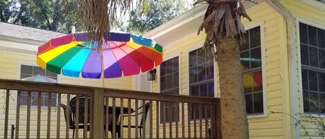 A covered patio with a colorful umbrella, a wooden deck, and a white fence.