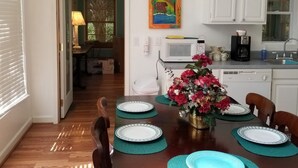 A dining area with a wooden table set for four, a vase of flowers, and a kitchen in the background.