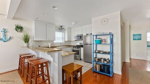 Una cocina con armarios blancos, un estante azul, taburetes de madera y una pequeña mesa de madera.