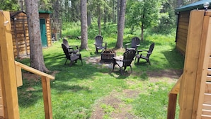 A wooden deck with Adirondack chairs and a fire pit, surrounded by a forested area.
