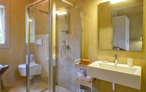 A bathroom with a glass-enclosed shower, a toilet, and a sink with a mirror above it.