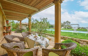Relax in a serene outdoor setting with a table for four, surrounded by wicker chairs and lush greenery overlooking a swimming pool.