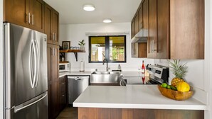 A modern kitchen with wooden cabinets, stainless steel appliances, and a central island with a fruit bowl. - BEST Ocean View in the Resort...Stunning & Panoramic!  Completely Renovated 2BR (Lihue)