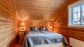 A cozy wooden cabin bedroom with a bed, two bedside lamps, and a window.
