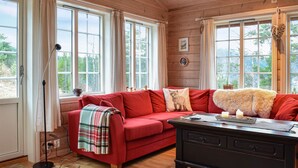 A cozy room with a red sofa, a black wooden table, and large windows with curtains.
