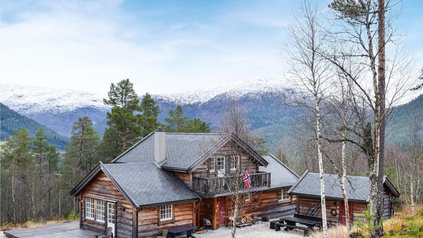 A log cabin with a deck, a covered porch, and a view of snow-capped mountains.