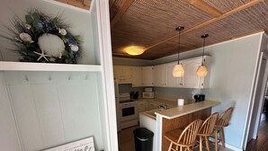 Une cuisine avec des meubles blancs, un îlot central en bois doté de tabourets, une pancarte « Bienvenue » et une guirlande décorative accrochée au mur.