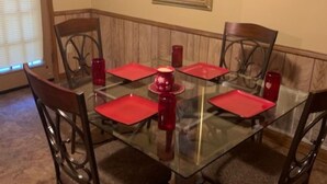 Une salle à manger avec une table en verre, des sets de table rouges et des chaises en bois.