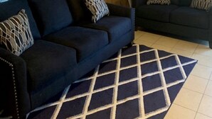 Un salon avec deux canapés sombres, un tapis à motifs, des murs recouverts de panneaux de bois et une grande œuvre d’art florale.
