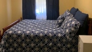 Une chambre à coucher avec un lit, un ventilateur de plafond, une fenêtre avec des rideaux et un tableau encadré au mur.