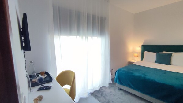 A hotel room with a bed, a desk with a chair, a TV, and a window with curtains.