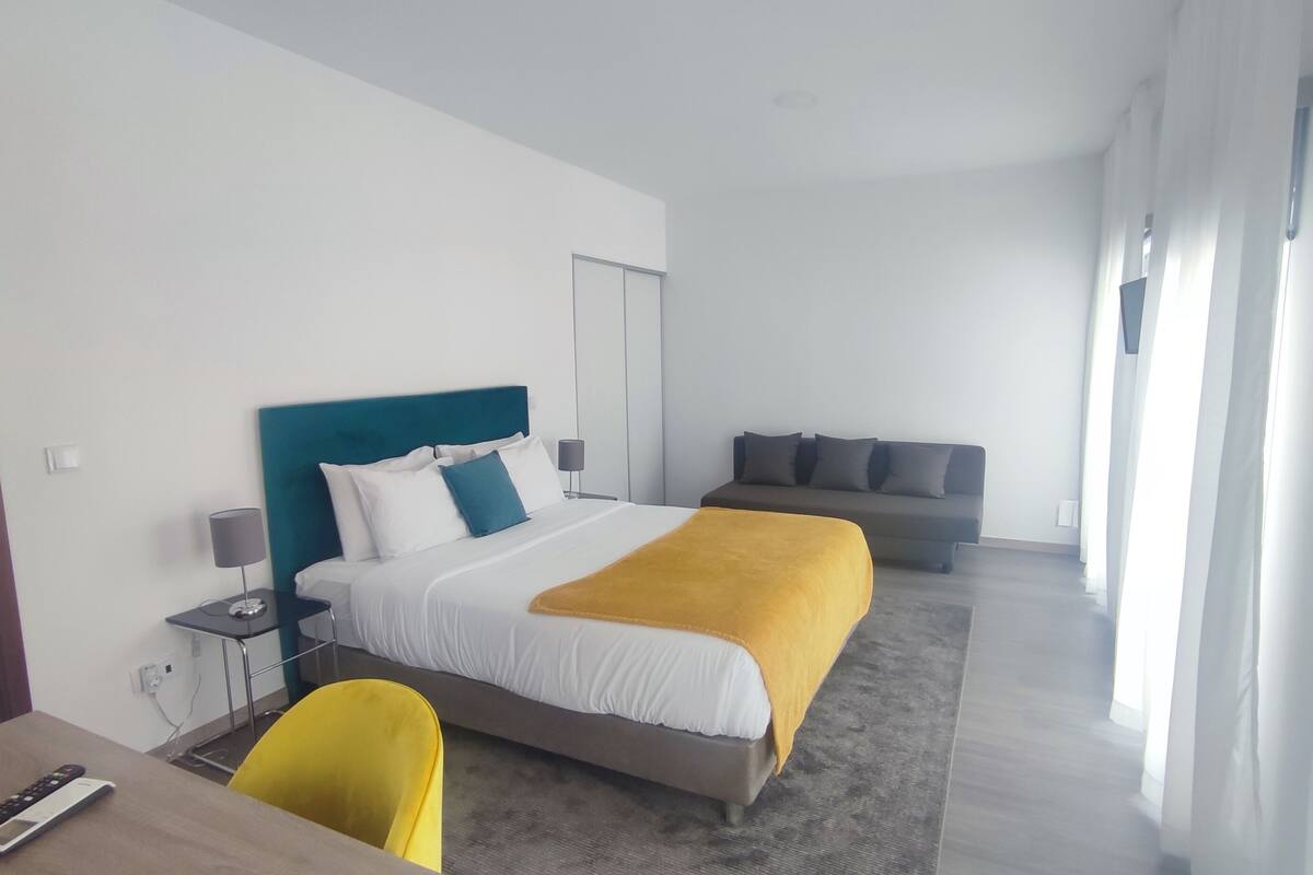 Una habitación de hotel moderna con una cama grande, un sofá, un escritorio con una silla y una ventana con cortinas.
