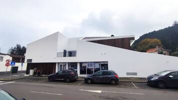 A modern building with a flat roof and a large glass entrance. There are cars parked in front and a stop sign visible.
