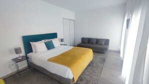 A modern hotel room with a large bed, a sofa, and a bedside table with a lamp.