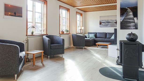 Een moderne woonkamer met een houten plafond, grote ramen, een grijze bank, een bijzettafeltje en een zwart fornuis.