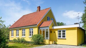 Een geel huis met een rood pannendak, witte ramen en een klein voortuintje.