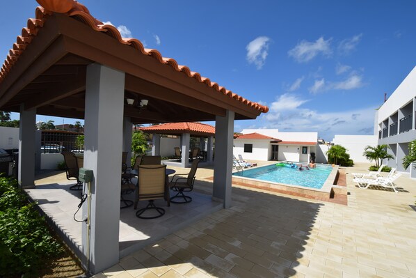 A covered outdoor area with a pool, lounge chairs, and a patio with tables and chairs.