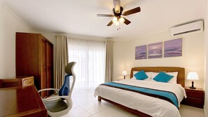 Une chambre d’hôtel équipée d’un lit, d’un bureau, d’une chaise, d’un ventilateur de plafond, d’un climatiseur et d’œuvres d’art accrochées au mur.