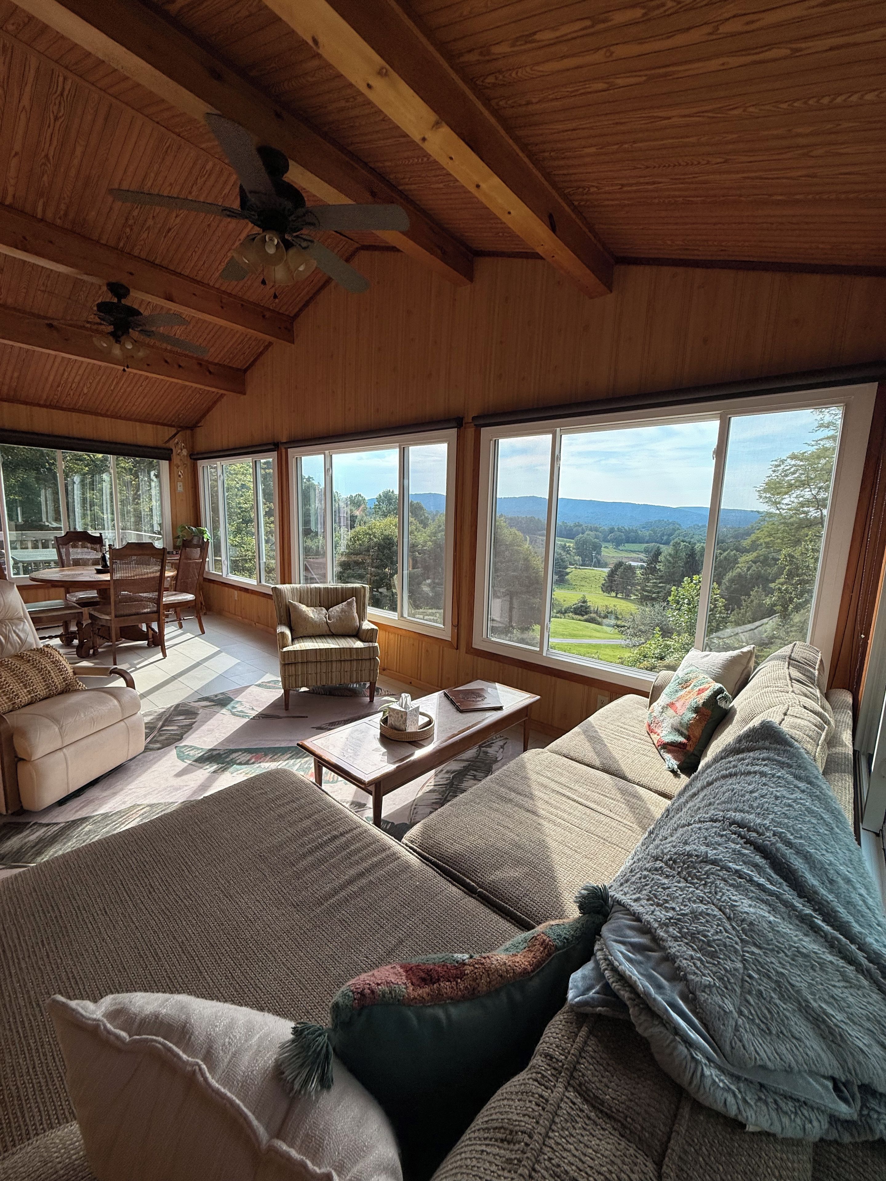 A spacious living room with a high ceiling, large windows, and a view of a forested landscape.