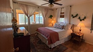 Une chambre à coucher avec un lit, deux tables de chevet avec des lampes, un ventilateur de plafond et une fenêtre avec des rideaux.