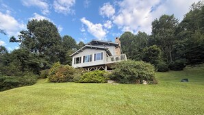 Une maison dotée d’un balcon, entourée d’une pelouse bien entretenue et d’arbres touffus.