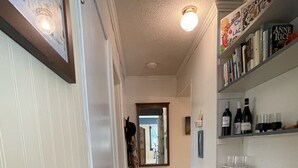 Un couloir doté d’un plancher en bois, d’une porte blanche, d’un miroir et d’une bibliothèque contenant des livres et des bouteilles de vin.