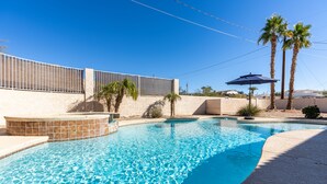 Una piscina con borde de azulejos, palmeras y zona delimitada por una valla.