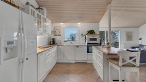 Una cocina moderna con armarios blancos, encimera de madera y vistas al exterior a través de un ventanal amplio.