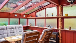Una habitación acogedora con una mesa de madera, dos sillas y un sofá. Hay ventanas con adornos y vistas a casas.