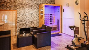 A sauna room with a stone wall, a wooden bench, a massage table, and an exercise bike.