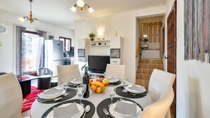 A dining area with a set table, chairs, a television, and a kitchen in the background.