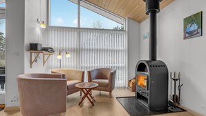 Ein modernes Wohnzimmer mit Kaminofen, gemütlicher Sitzgelegenheit und großen Fenstern.