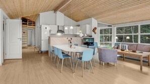 Eine moderne Küche mit weißen Schränken, einer Holzbalkendecke und einem Essbereich mit blauen Stühlen und einem runden Tisch.