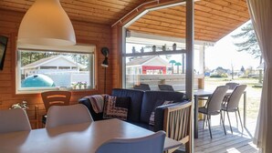 Un interior acogedor con techo de madera, un sofá, una mesa de comedor y sillas. Hay un ventanal grande que ofrece vistas al exterior.