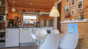 Una cocina compacta con electrodomésticos blancos, una zona de comedor con sillas blancas y paredes de madera.