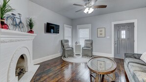 Un salon avec une cheminée, deux fauteuils, une table basse et un ventilateur de plafond.