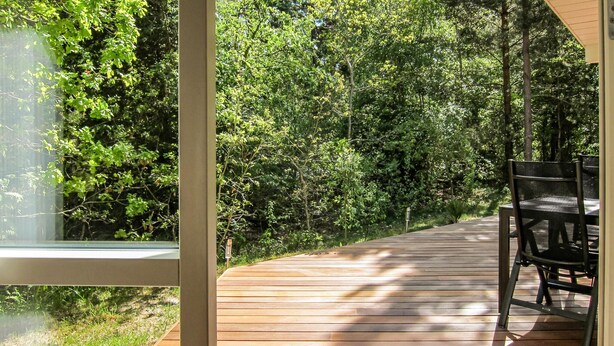 Una terraza de madera con una mesa y sillas, rodeada de abundante vegetación.