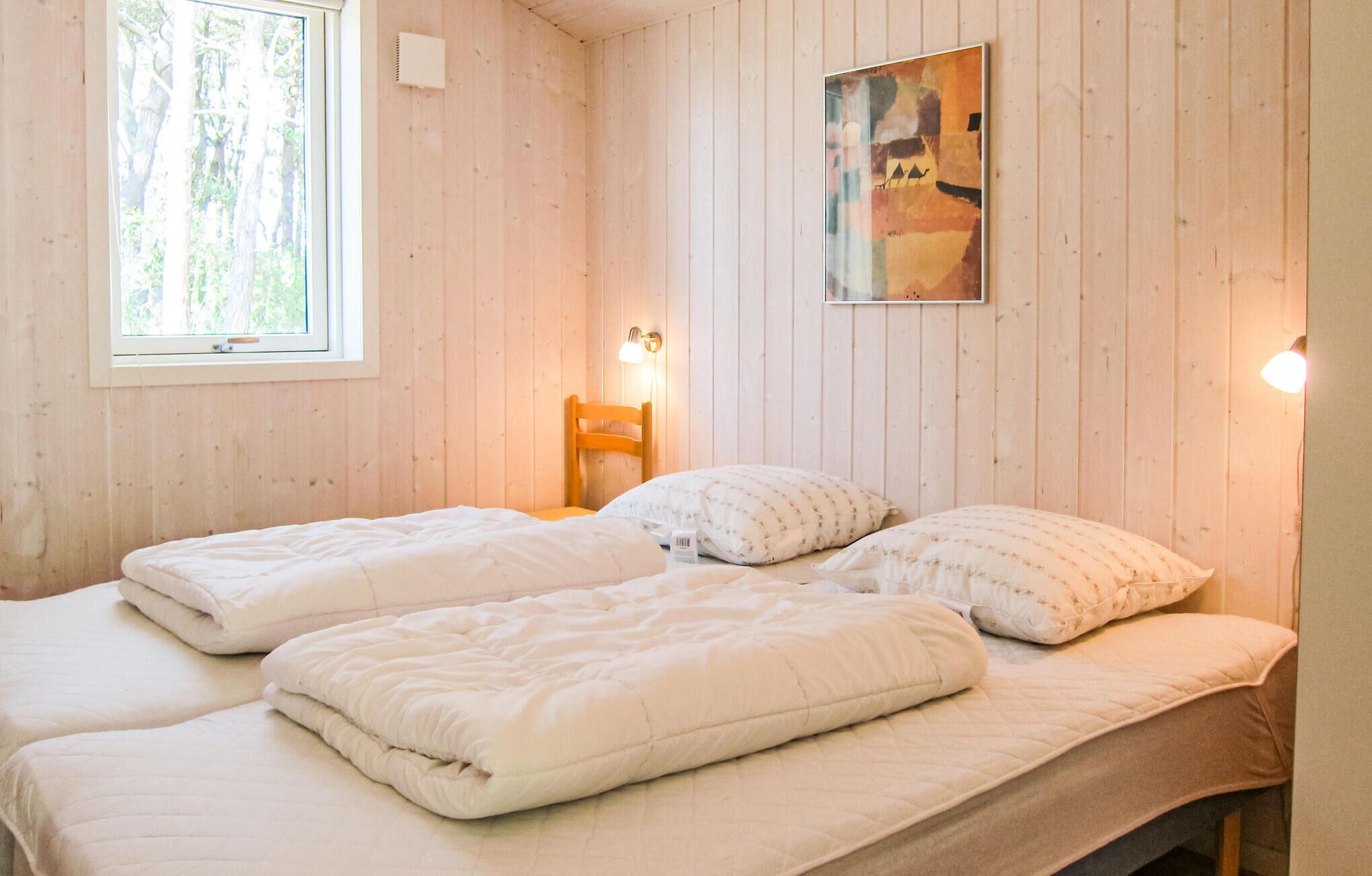 Quarto com duas camas, janela, pintura e luminária na parede.